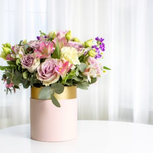 Beautiful bouquet of flowers in pink hat box on white table. Floral arrangement.