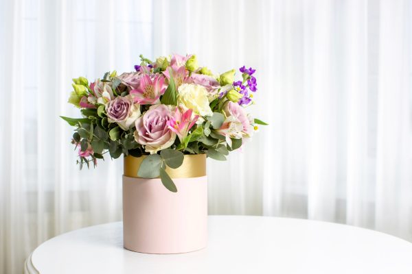 Beautiful bouquet of flowers in pink hat box on white table. Floral arrangement.